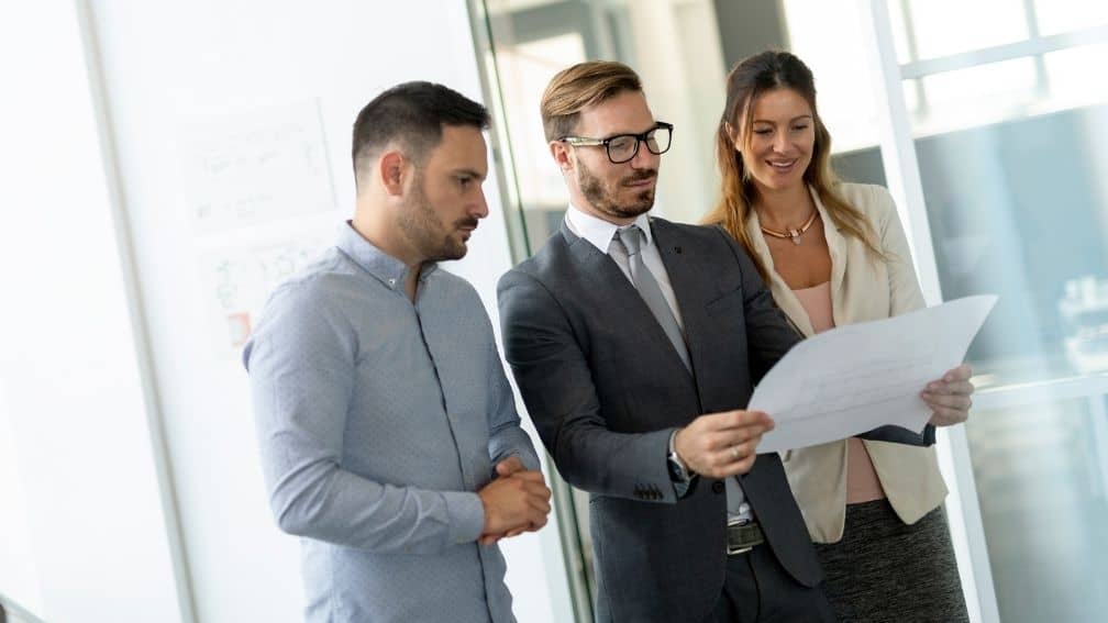 Man looking at real estate blueprints next to colleagues